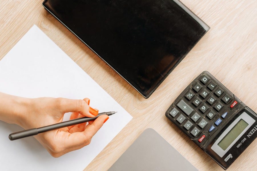Person writing figures into a ledger at a desk